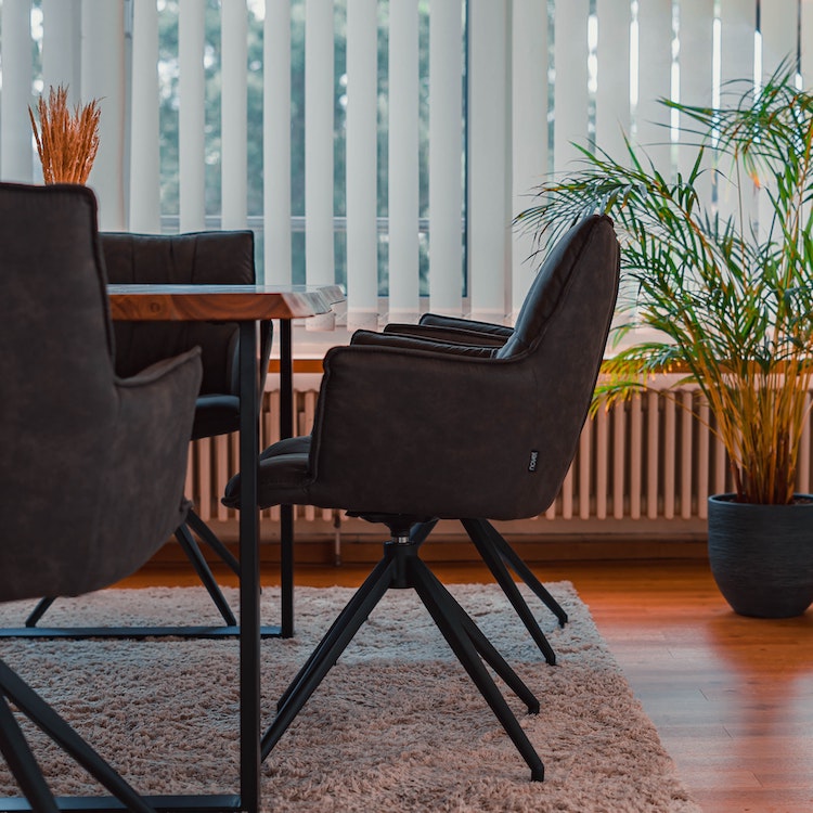 Dark brown chair next to a wooden dining table, with plants and blinds in the background